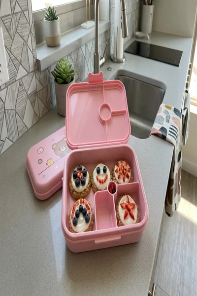 Lonchera rosada con galletas de avena decoradas con caritas y flores de fruta